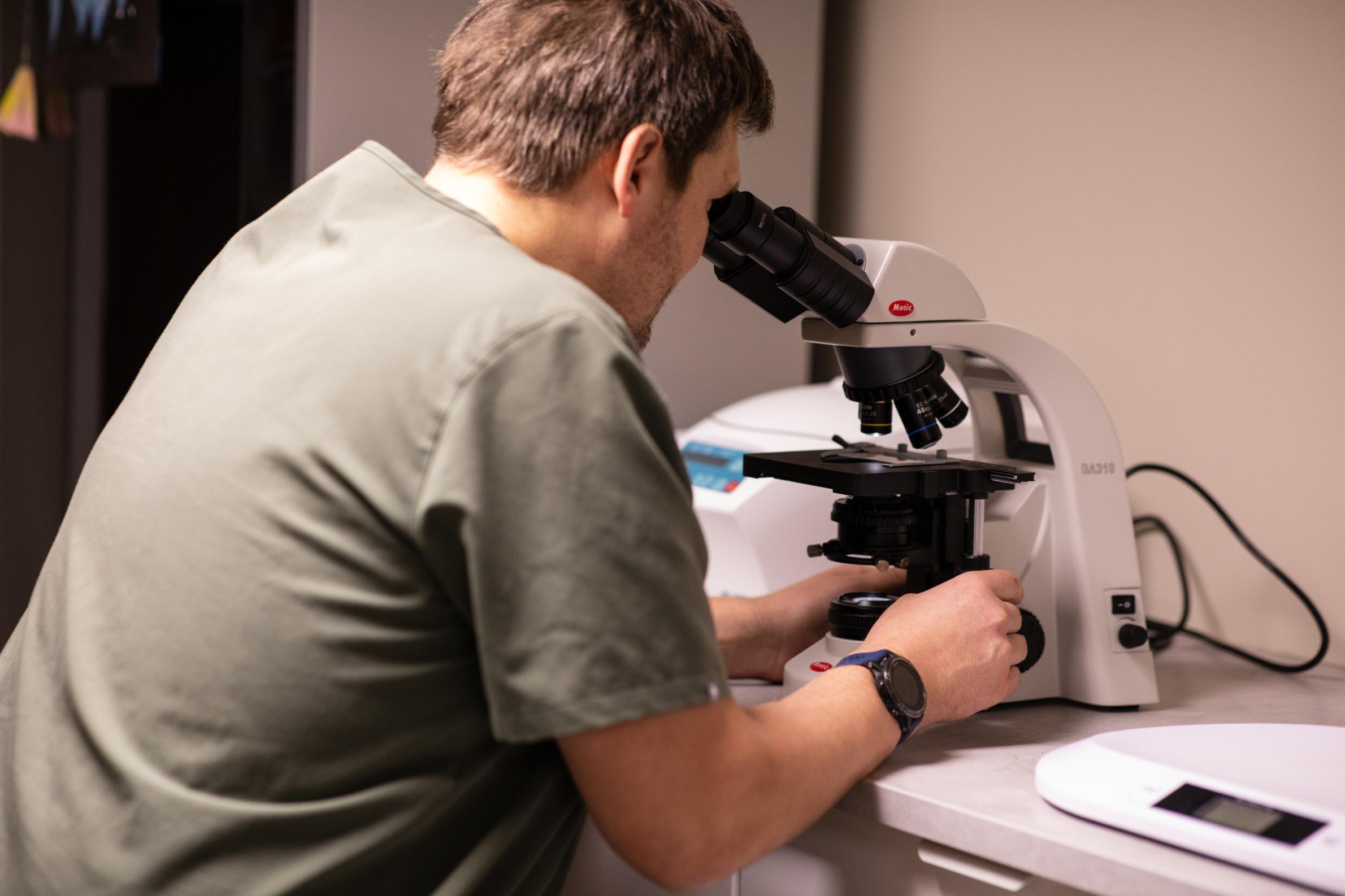 Mann ser gjennom mikroskop